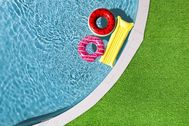 Image of Inflatable rings and mattress floating in swimming pool surrounded by green grass, top view