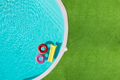 Image of Inflatable rings and mattress floating in swimming pool surrounded by green grass, top view