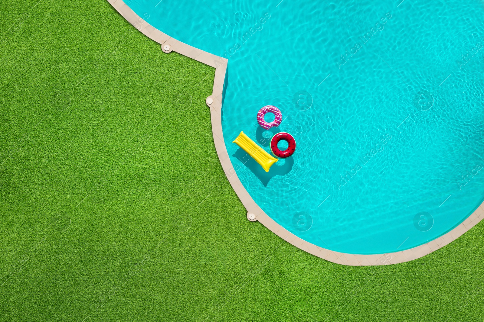 Inflatable rings and mattress floating in swimming pool surrounded by green grass, top view Image of Inflatable rings and mattress floating in swimming pool surrounded by green grass, top view