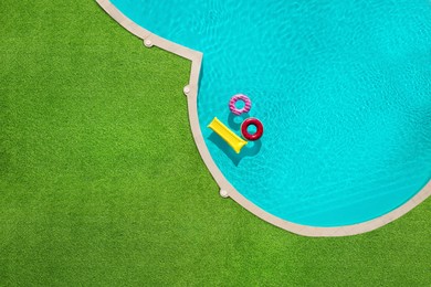 Image of Inflatable rings and mattress floating in swimming pool surrounded by green grass, top view