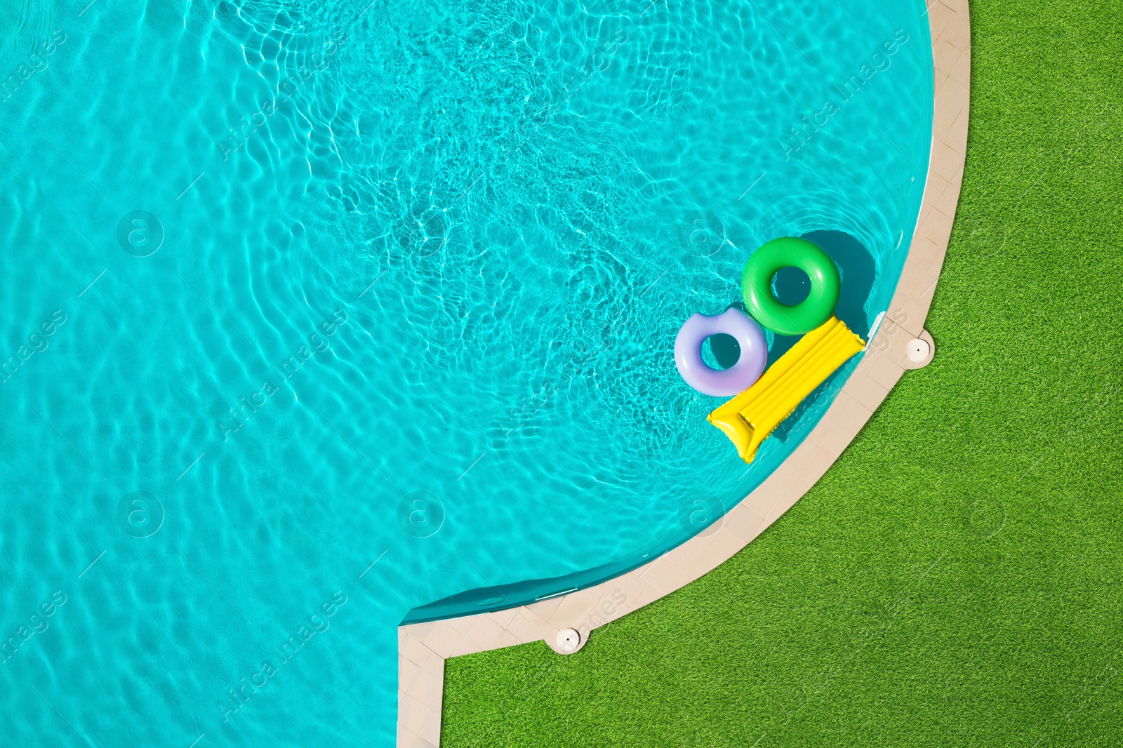 Image of Inflatable rings and mattress floating in swimming pool surrounded by green grass, top view