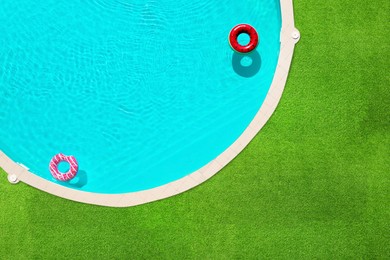 Image of Inflatable rings floating in swimming pool surrounded by green grass, top view
