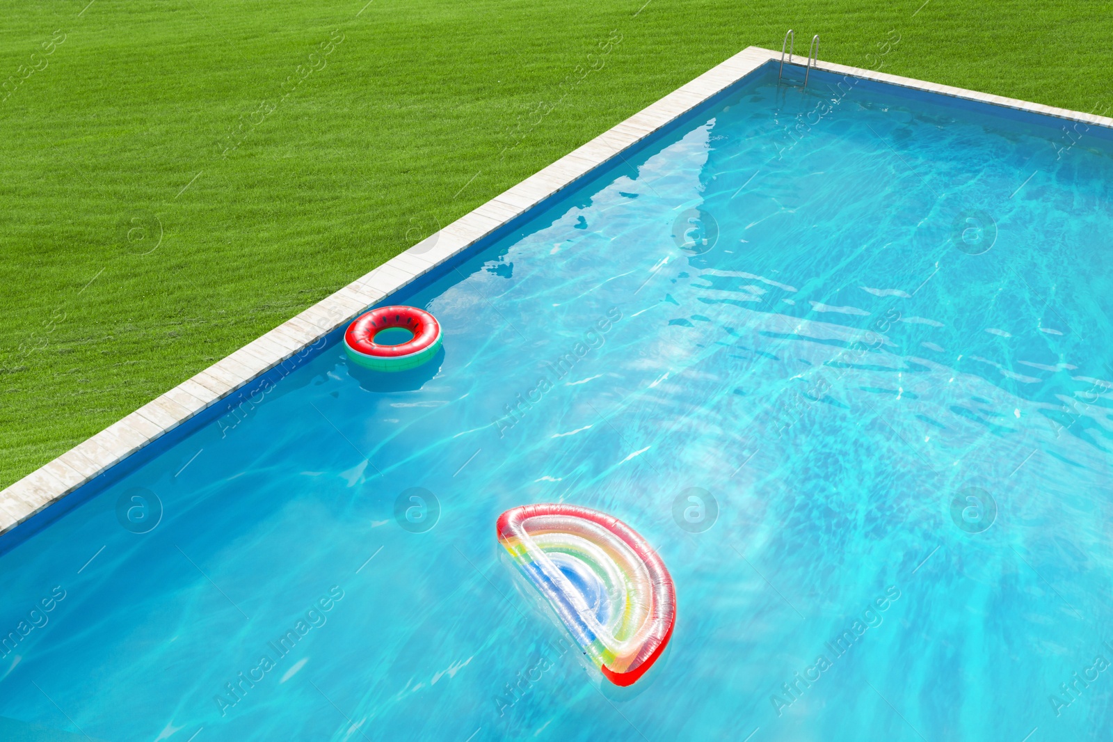 Inflatable ring and mattress floating in swimming pool surrounded by green grass Image of Inflatable ring and mattress floating in swimming pool surrounded by green grass