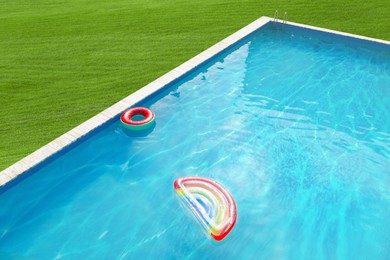 Image of Inflatable ring and mattress floating in swimming pool surrounded by green grass