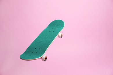 Image of Turquoise skateboard in air against pink background. Space for text