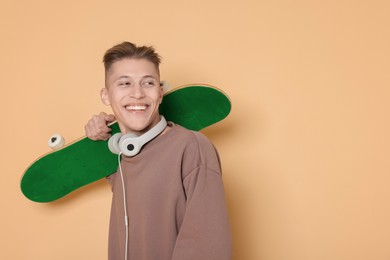 Image of Happy man with green skateboard and headphones on beige background. Space for text