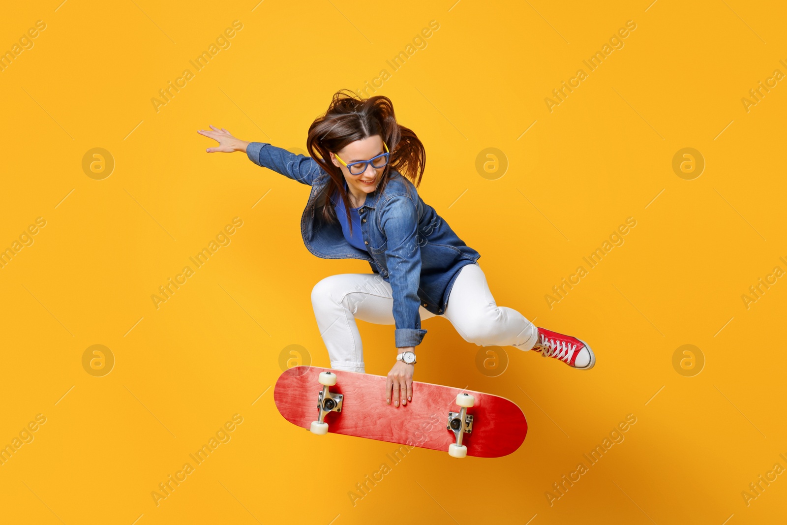 Smiling woman jumping with red skateboard on orange background Image of Smiling woman jumping with red skateboard on orange background