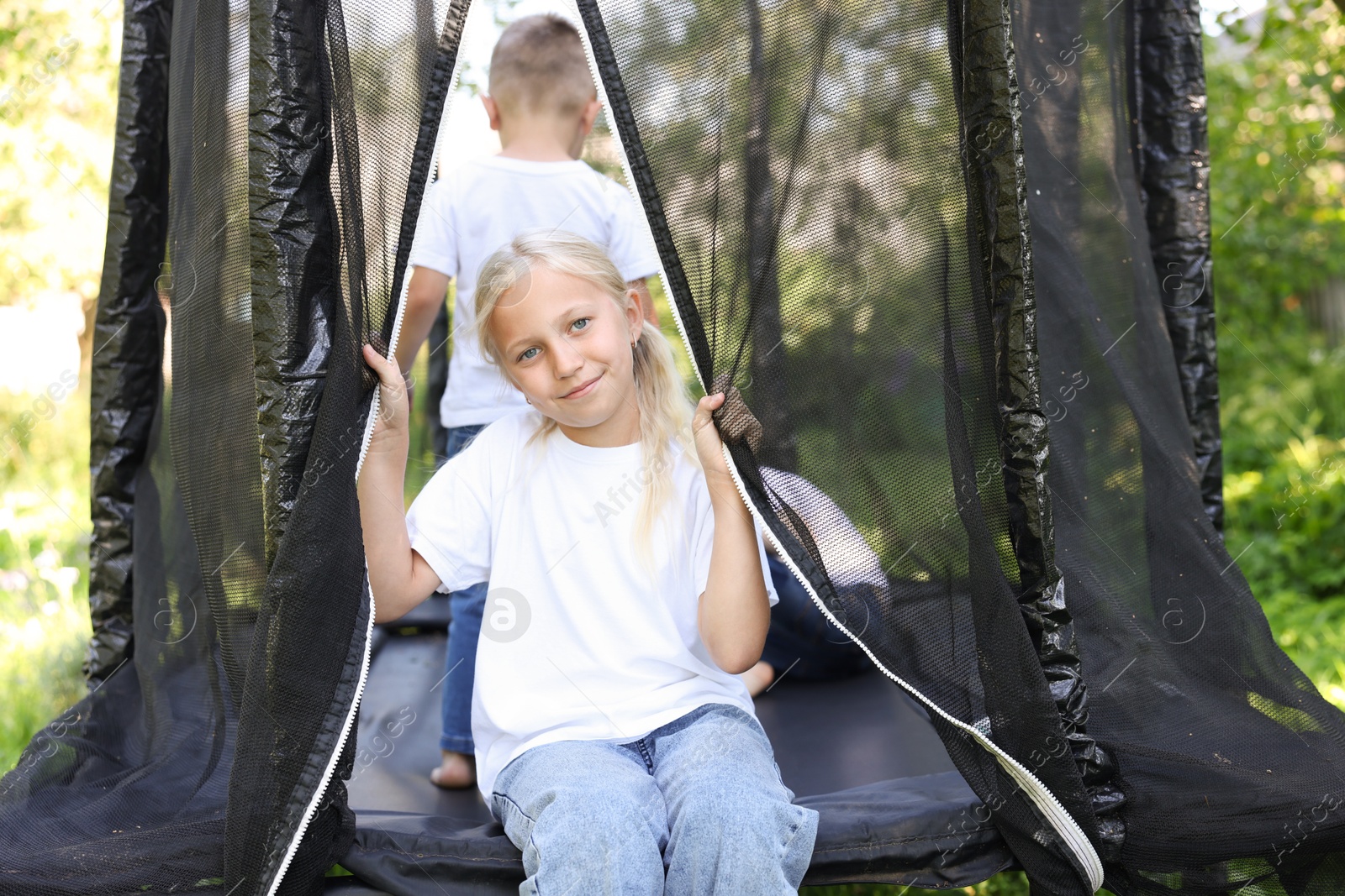 Photo of Cute little girl and her friends on black trampoline outdoors