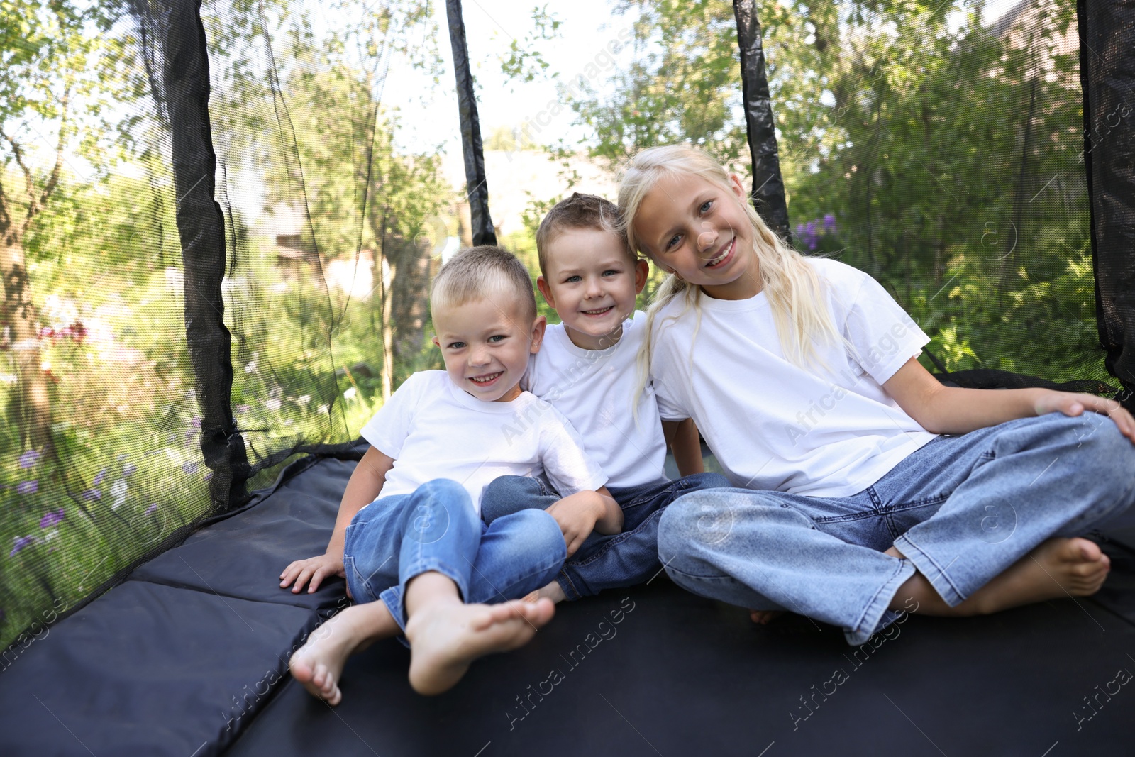 Photo of Happy children sitting on black trampoline outdoors
