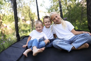 Photo of Happy children sitting on black trampoline outdoors