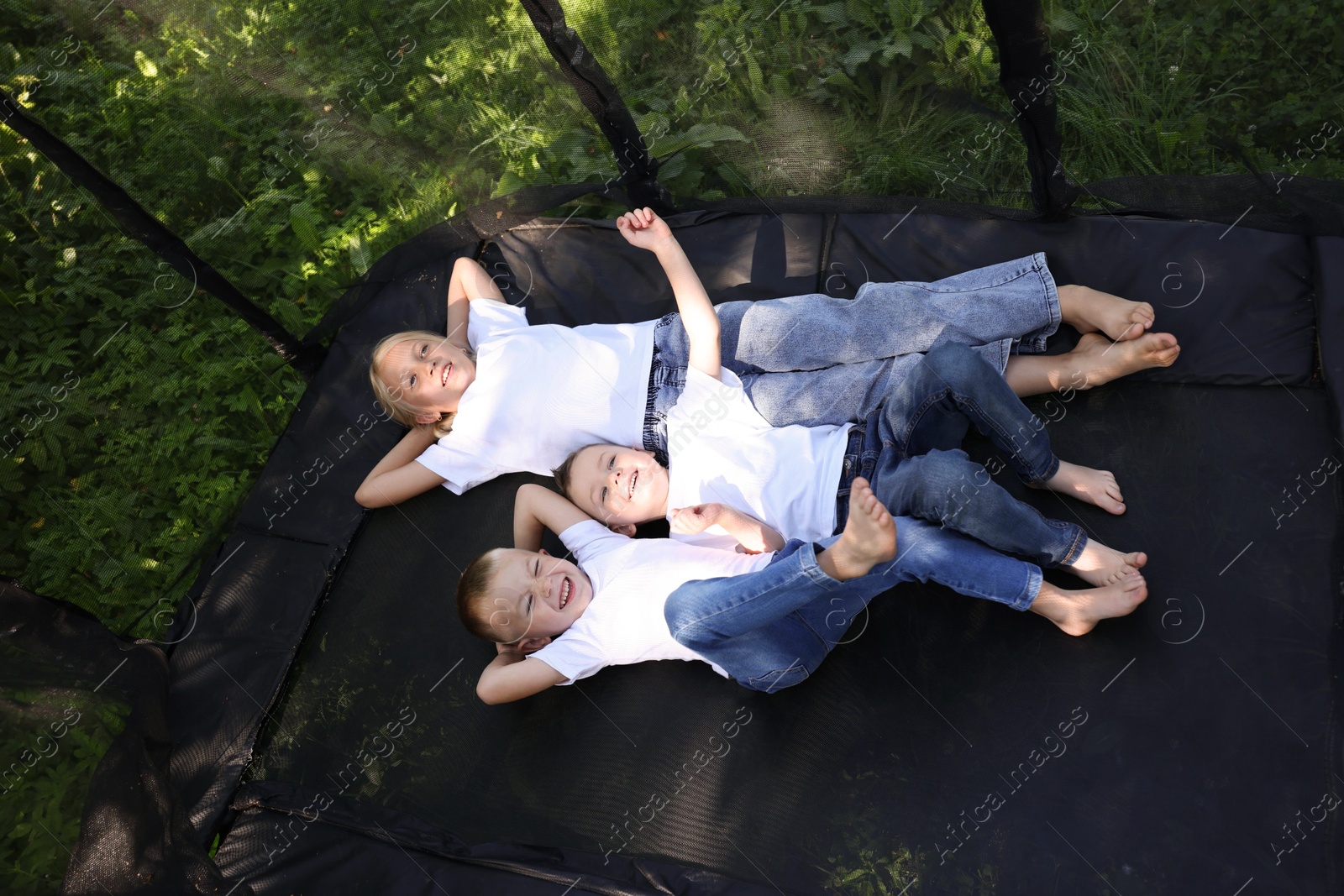 Photo of Happy children lying on black trampoline outdoors, above view