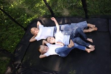 Photo of Happy children lying on black trampoline outdoors, above view