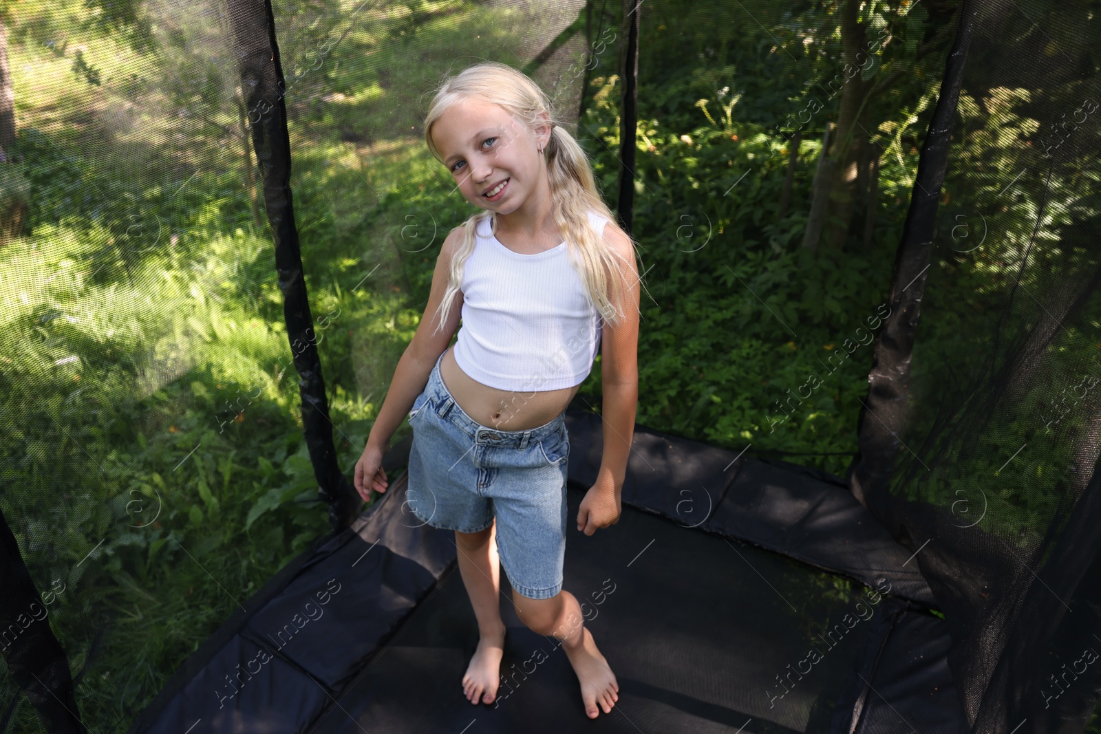 Photo of Happy little girl on black trampoline outdoors