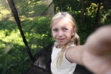 Photo of Cute little girl taking selfie on black trampoline outdoors. Space for text