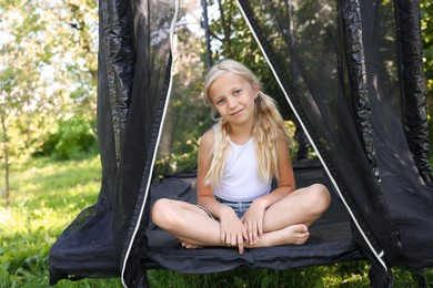 Photo of Cute little girl sitting on black trampoline outdoors