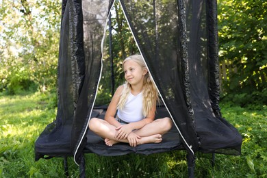 Photo of Cute little girl sitting on black trampoline outdoors
