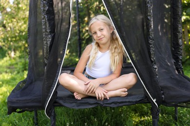 Photo of Cute little girl sitting on black trampoline outdoors