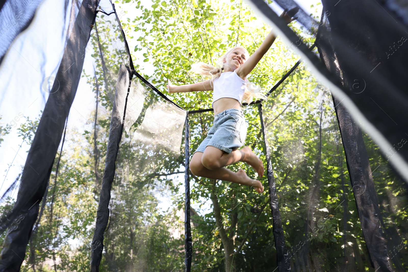 Happy little girl jumping on black trampoline outdoors, low angle view Photo of Happy little girl jumping on black trampoline outdoors, low angle view