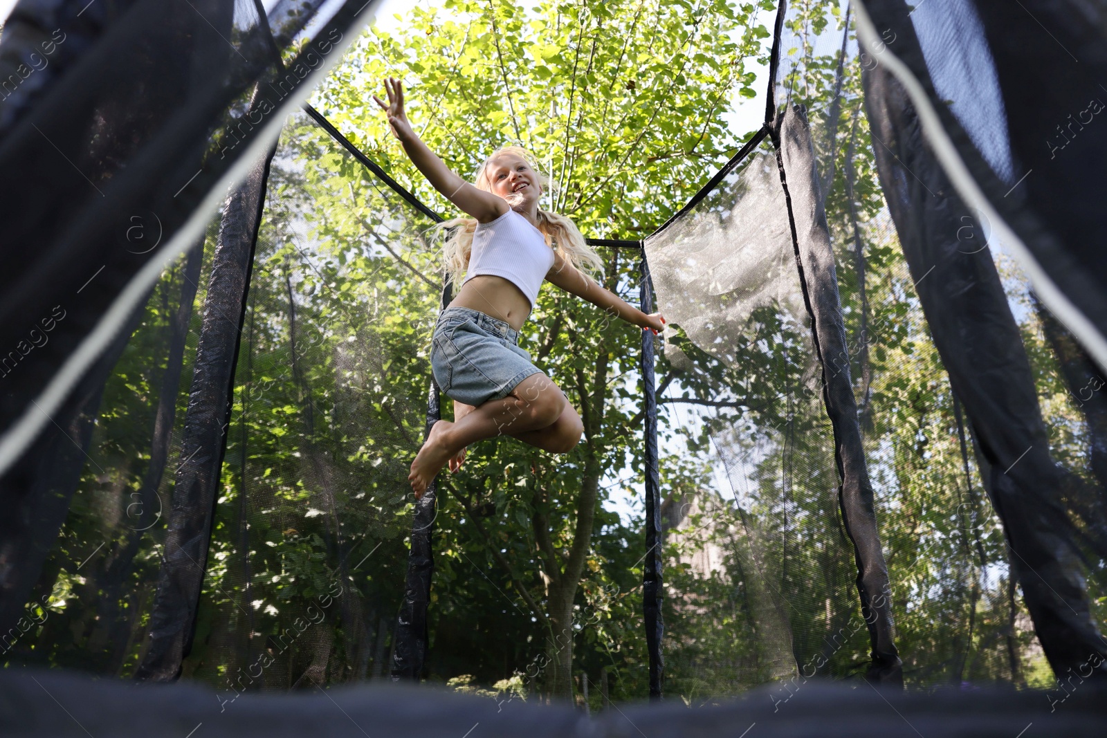 Happy little girl jumping on black trampoline outdoors, low angle view Photo of Happy little girl jumping on black trampoline outdoors, low angle view