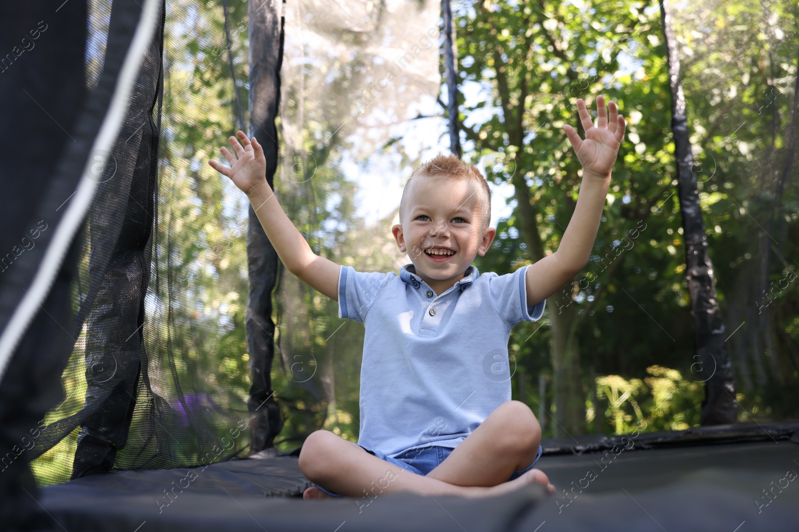 Happy little boy sitting on black trampoline outdoors Photo of Happy little boy sitting on black trampoline outdoors