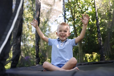 Photo of Happy little boy sitting on black trampoline outdoors