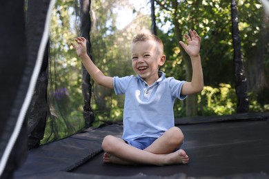 Photo of Happy little boy sitting on black trampoline outdoors