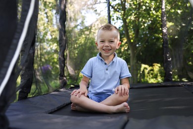 Photo of Happy little boy sitting on black trampoline outdoors