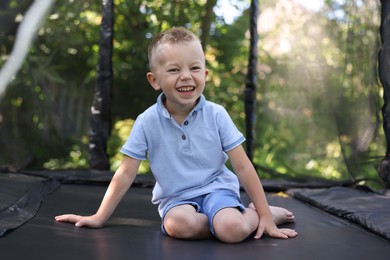 Photo of Happy little boy posing on black trampoline outdoors