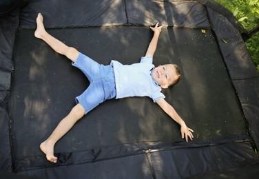 Photo of Happy little boy lying on black trampoline outdoors, above view
