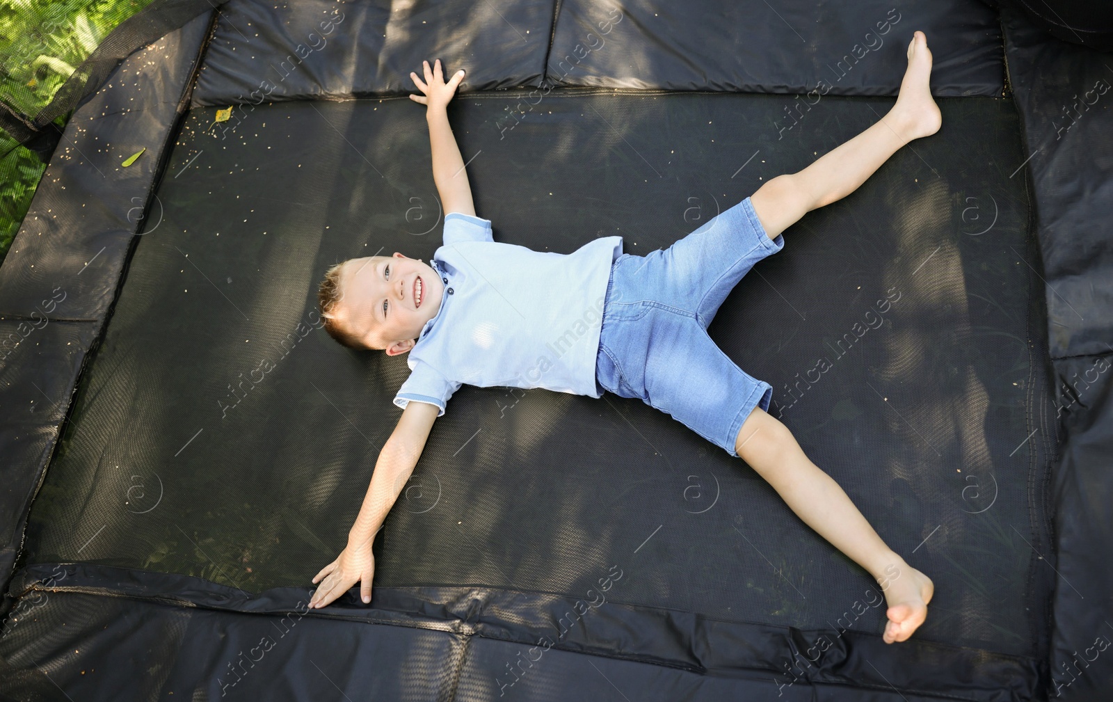 Photo of Happy little boy lying on black trampoline outdoors, above view