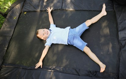 Photo of Happy little boy lying on black trampoline outdoors, above view