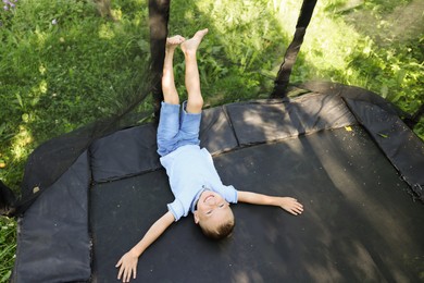 Photo of Happy little boy lying on black trampoline outdoors, above view