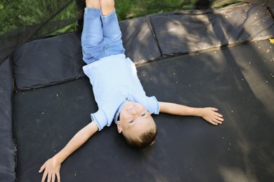 Photo of Happy little boy lying on black trampoline outdoors, above view