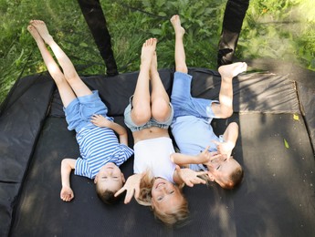 Photo of Happy children lying on black trampoline outdoors, above view