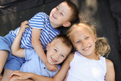 Photo of Happy children lying on black trampoline, top view