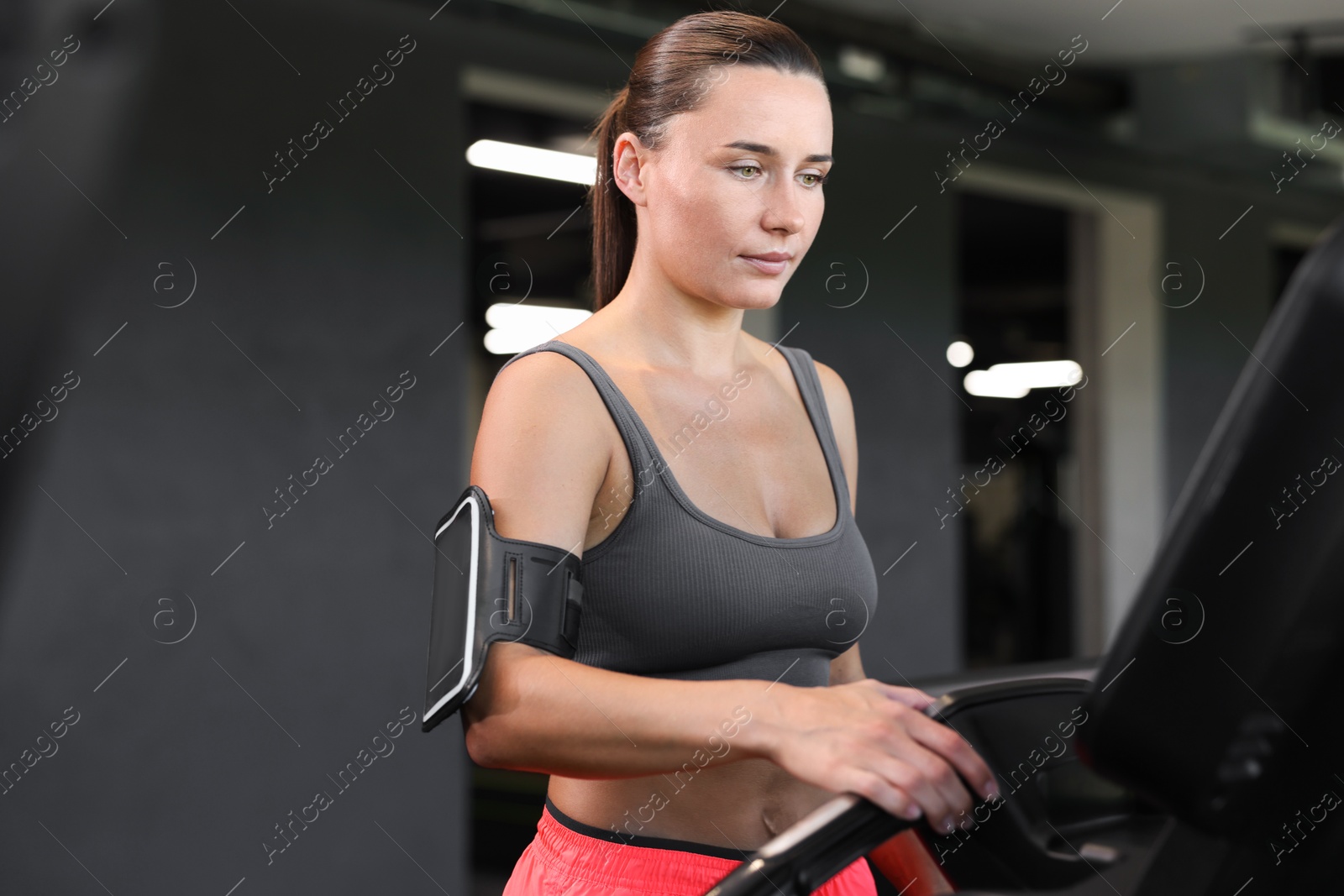 Photo of Athletic woman with armband training on treadmill in gym