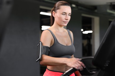Photo of Athletic woman with armband training on treadmill in gym