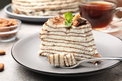 Photo of Piece of tasty crepe cake with cocoa powder, chocolate and nuts served on light table, closeup
