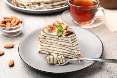 Photo of Piece of tasty crepe cake with cocoa powder, chocolate and nuts served on light table, closeup