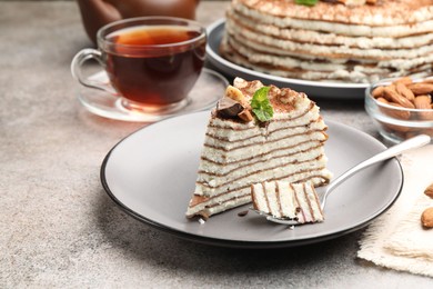 Photo of Piece of tasty crepe cake with cocoa powder, chocolate and nuts served on light table, closeup