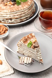 Photo of Piece of tasty crepe cake with cocoa powder, chocolate and nuts served on light table, closeup