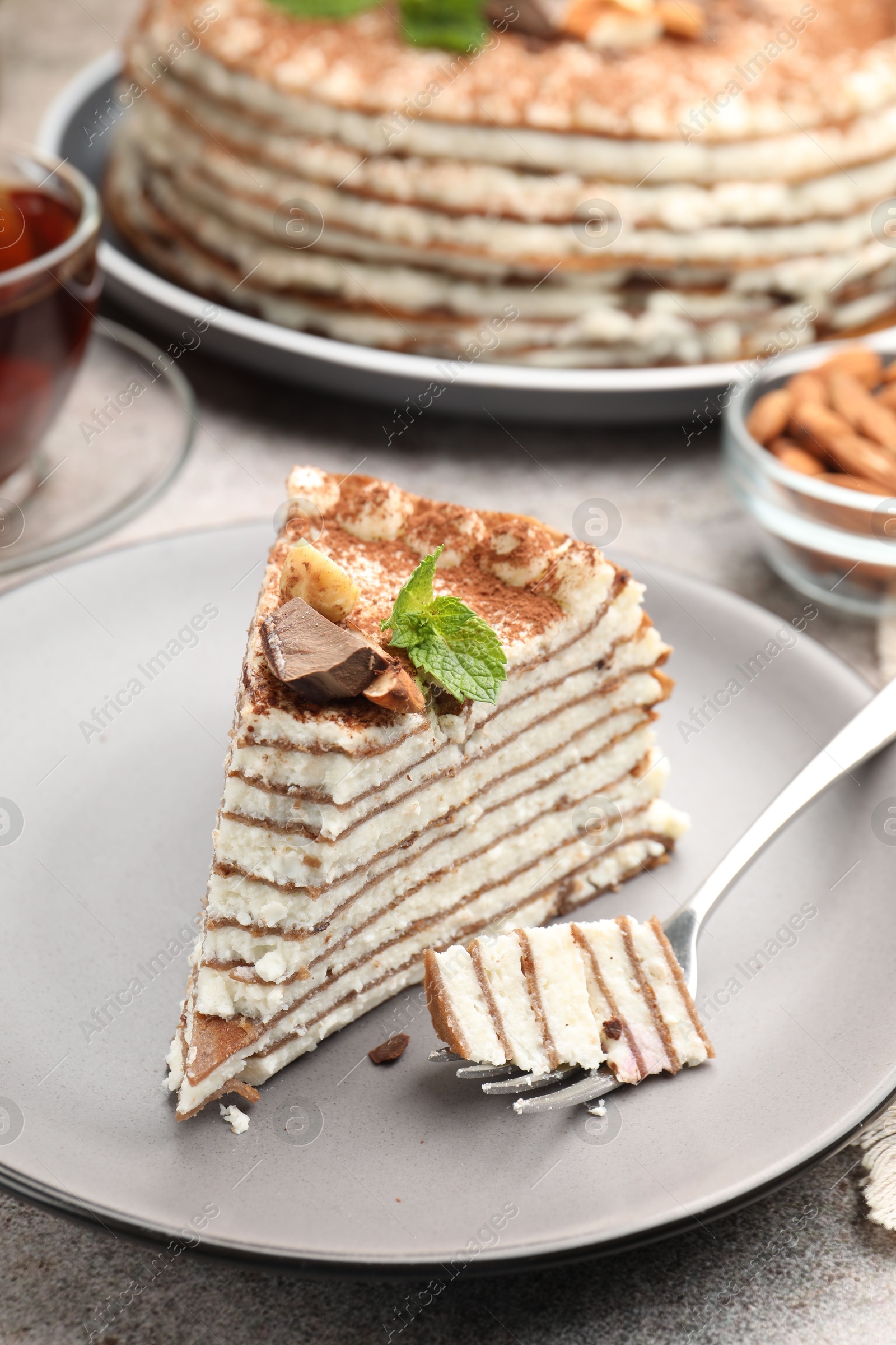 Photo of Piece of tasty crepe cake with cocoa powder, chocolate and nuts served on light table, closeup