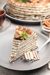 Photo of Piece of tasty crepe cake with cocoa powder, chocolate and nuts served on light table, closeup