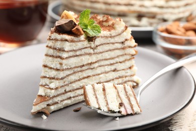 Photo of Piece of tasty crepe cake with cocoa powder, chocolate and nuts served on light table, closeup
