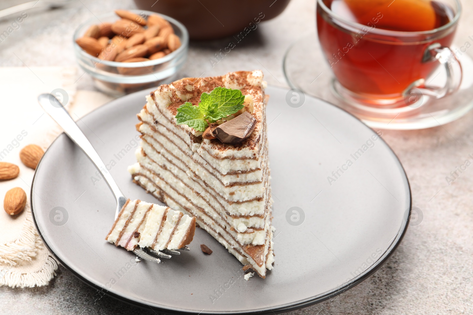 Photo of Piece of tasty crepe cake with cocoa powder, chocolate and nuts served on light table, closeup