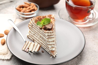 Photo of Piece of tasty crepe cake with cocoa powder, chocolate and nuts served on light table, closeup