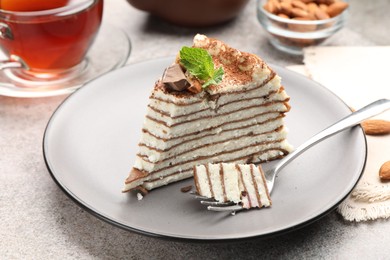 Photo of Piece of tasty crepe cake with cocoa powder, chocolate and nuts served on light table, closeup