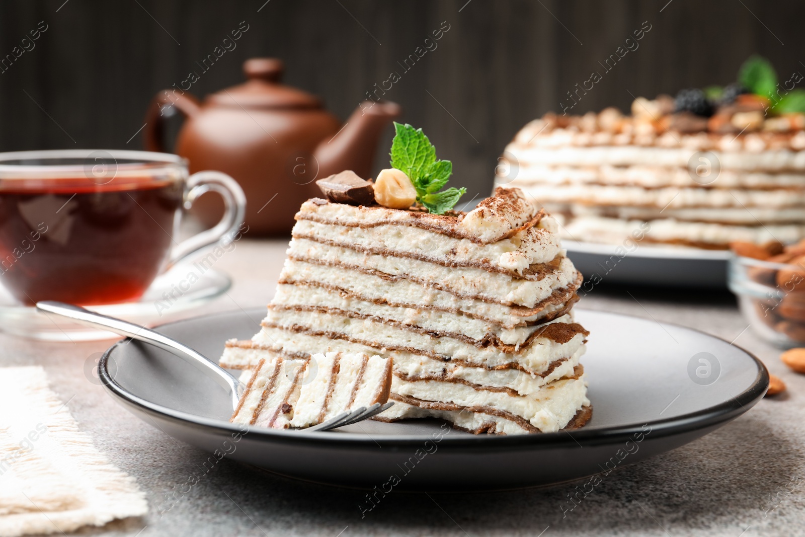Photo of Piece of tasty crepe cake with cocoa powder, chocolate and nuts served on light table, closeup