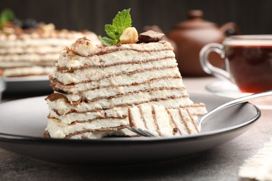 Photo of Piece of tasty crepe cake with cocoa powder, chocolate and nuts served on light table, closeup