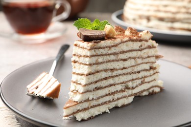 Photo of Piece of tasty crepe cake with cocoa powder, chocolate and nuts served on light table, closeup